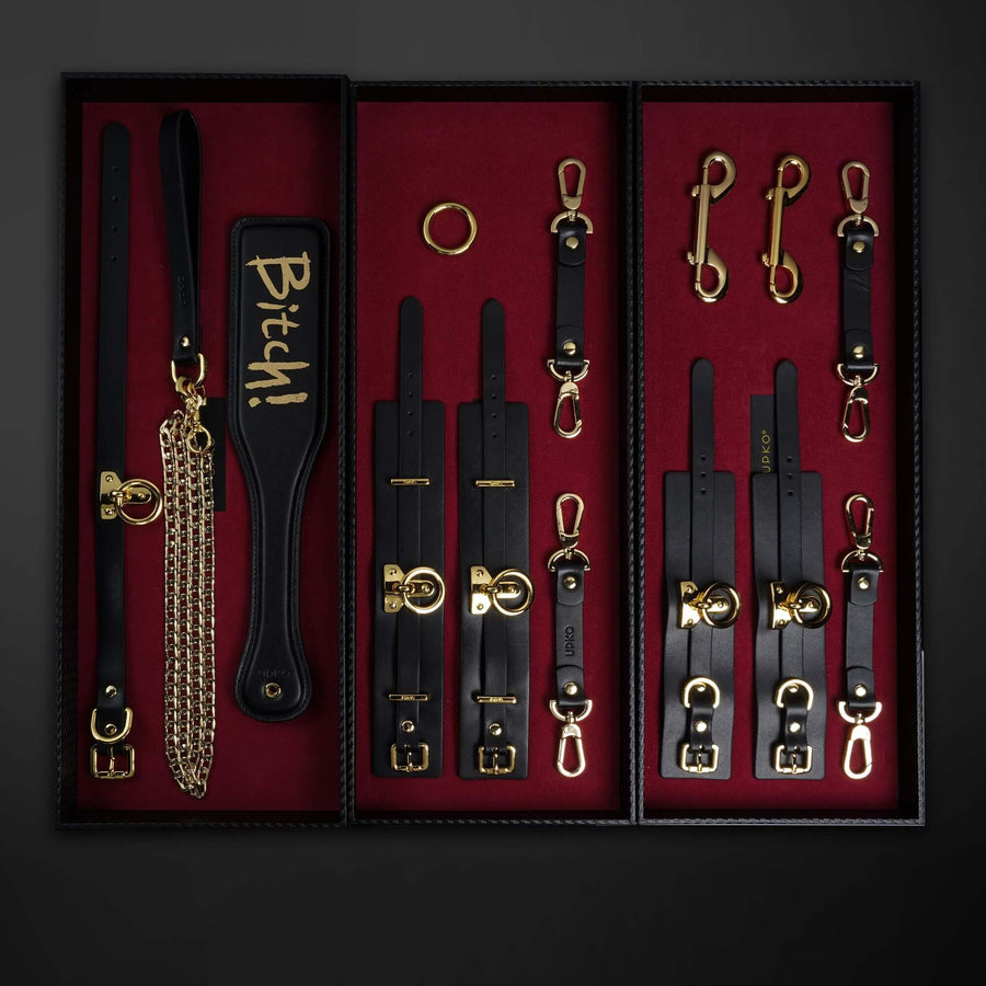 Luxury Italian leather bondage tools set in black with gold accents and red lining, featuring collar, leash, and cuffs.