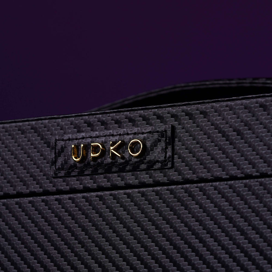 Close-up of UPKO branded black carbon fiber surface with gold lettering on a purple background.