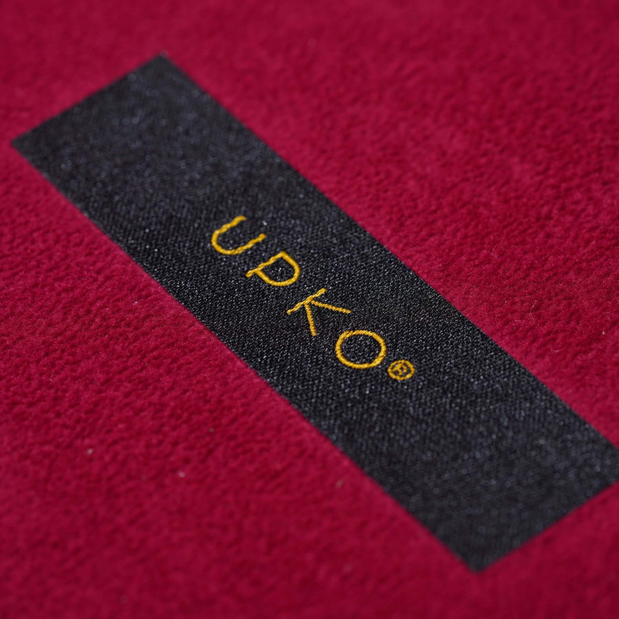 Close-up of UPKO logo on a soft red fabric background, showcasing brand detail and texture.