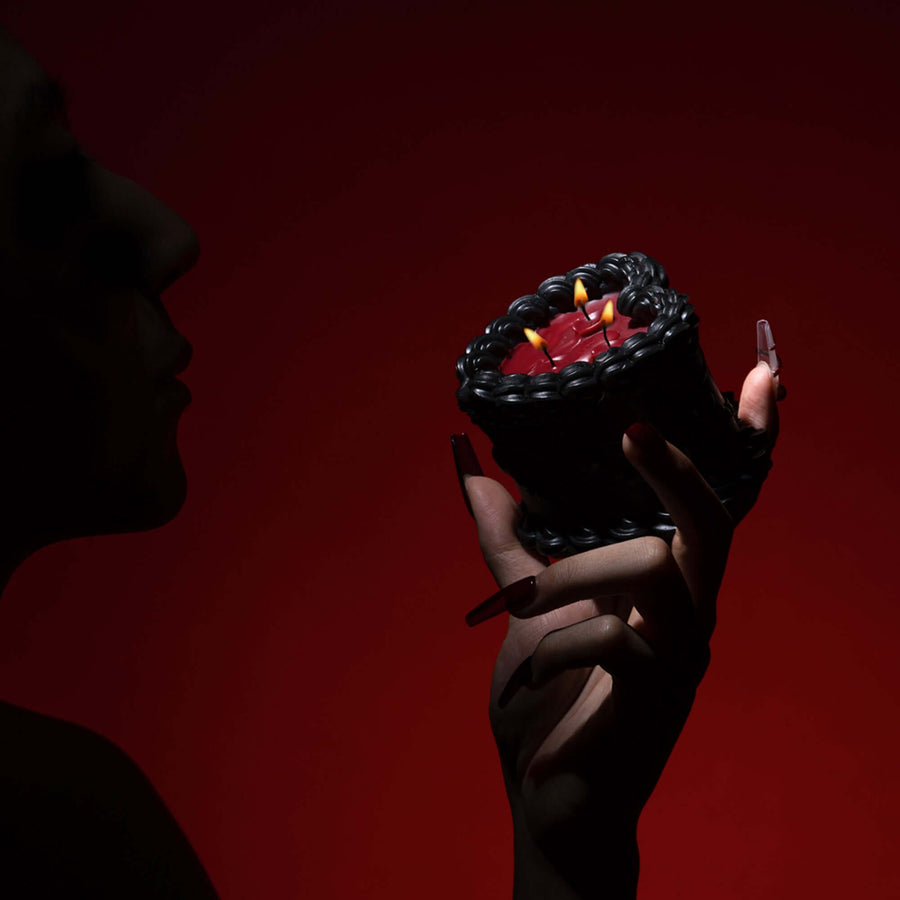 Woman holding a black and red low-temperature wax candle with a cake design against a dark red background.