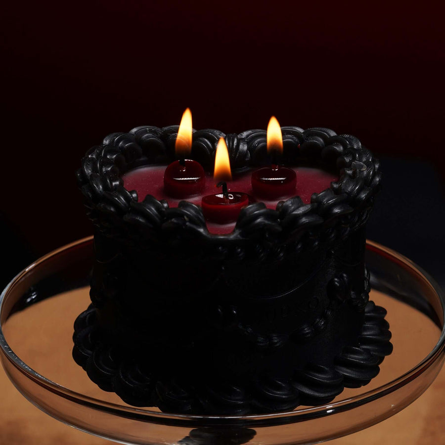 Low-temperature wax candle designed as a cake, featuring three flames and a classic red-and-black color scheme.